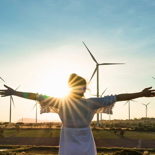 Wind turbines farm is an alternative electricity source, Concept of sustainable resources, Renewable energy concept, Girl standing and watching the sunset with wind generators turbines to backgrounds.